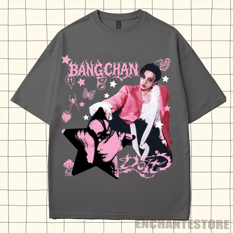 Pu&ograve; includere: T-shirt grigio con un design grafico rosa e nero. Il design include il testo "BANGCHAN", un ritratto, stelle e altri elementi decorativi. La maglietta &egrave; in stile casual.