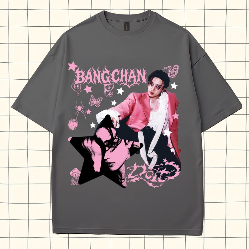 Pode incluir: Uma camiseta cinza com um design gr&aacute;fico rosa com o texto "BANGCHAN" e um retrato de uma pessoa com um casaco rosa. O design inclui estrelas, borboletas e outros elementos decorativos.