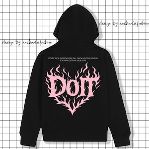 Puede incluir: Sudadera con capucha negra con un dise&ntilde;o en forma de coraz&oacute;n rosa con la palabra "Dom". El texto "STRAY KIDS EVERYWHERE ALL AROUND THE WORLD YOU MAKE STRAY KIDS STAY" est&aacute; encima del coraz&oacute;n. Las palabras "design by enchante fashion" est&aacute;n arriba a la izquierda y a la derecha.