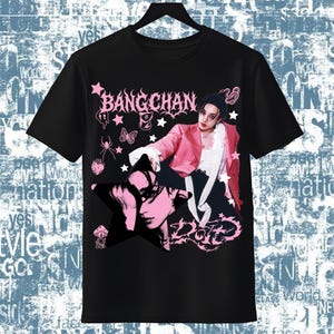 Pode incluir: T-shirt preto com um design gr&aacute;fico rosa com o texto "BANGCHAN" e um retrato. O design apresenta estrelas, borboletas e a palavra "DOTE". A pessoa na camiseta usa um blazer rosa.