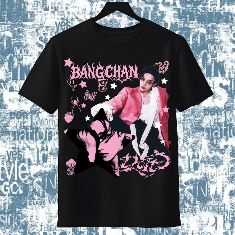 Pode incluir: T-shirt preto com um design gr&aacute;fico rosa com o texto "BANGCHAN" e um retrato. O design apresenta estrelas, borboletas e a palavra "DOTE". A pessoa na camiseta usa um blazer rosa.
