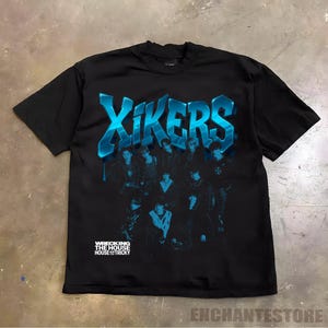 May include: Black t-shirt with a blue gradient graphic of the word "XIKERS" and a group of people. The text "WRECKING THE HOUSE HOUSE TRICKY" is printed below the group. The shirt is a crew neck.