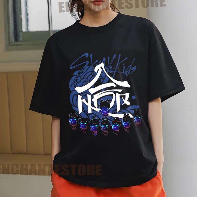 Może przedstawiać: Czarny T-shirt z nadrukiem graficznym koreańskiego boysbandu Stray Kids. Grafika przedstawia nazwę zespołu w języku koreańskim i angielskim, a także stylizowany wizerunek członk&oacute;w zespołu.