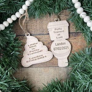 May include: Two wooden Christmas ornaments shaped like a toilet and a pile of poop. The toilet ornament says "Potty Trained at Last Landon 07/02/2021". The poop ornament says "Little Shit is Potty Trained! Landon 07/02/2021".