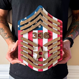 May include: A wooden plaque with a red, white, and blue American flag design. The plaque features a stylized military rank insignia with five chevrons and a star. The number "336" is displayed on the plaque.