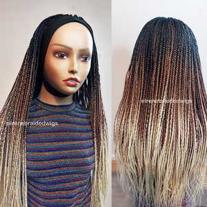 May include: A long, ombre braided wig with black, brown, and blonde hair. The wig is styled in a straight, sleek style and is worn on a mannequin head. The wig is made with synthetic hair and is available for purchase.