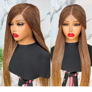 May include: A long, braided wig in shades of brown and light brown, styled with a side parting. The wig is displayed on a mannequin head wearing a black top, highlighting the detailed braid work and colour gradient.