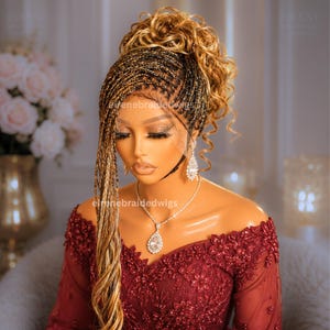 May include: A braided wig with a lace front, featuring a mix of black and blonde braids. The wig is styled with a high bun and loose curls. The model is wearing a burgundy off-the-shoulder dress and diamond jewelry. The text "eirenebraidedwigs" is visible.
