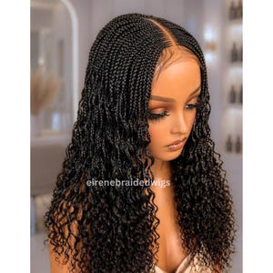 Puede incluir: Una peluca trenzada negra con textura rizada. La peluca presenta una raya en medio y está peinada con pequeñas trenzas apretadas que se transforman en rizos sueltos y voluminosos. El texto "eirenebraidedwigs" es visible.