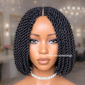 May include: A woman with a black braided bob wig. The wig is styled in a short, shoulder-length cut with a center part. The woman is wearing a silver necklace. The text "eirenebraidedwigs" is visible.