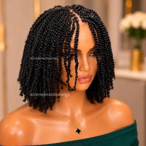 May include: A black, short, braided wig with a natural-looking hairline. The wig features individual twists, creating a textured appearance. The model is wearing a green off-the-shoulder top and a gold necklace with a black clover pendant. The text "eirenebraidedwigs" is visible.