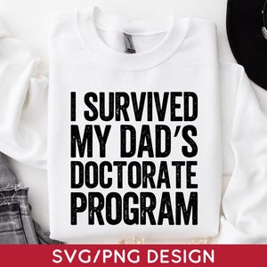 May include: White sweatshirt with the text "I SURVIVED MY DAD'S DOCTORATE PROGRAM" in bold black letters. The bottom of the image has the text "SVG/PNG DESIGN" in white letters on a red background. A black hat and jeans are in the background.