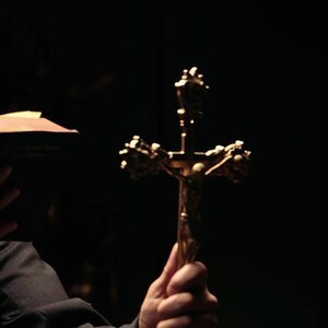 Könnte beinhalten: Eine Person hält ein goldenes Kruzifix mit einer Jesus Christus-Figur darauf. Das Kruzifix ist scharf, während das Gesicht der Person im Schatten verborgen ist.