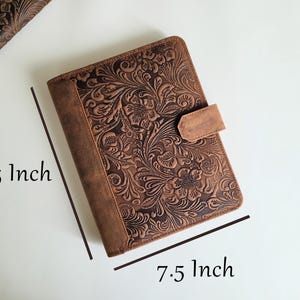 Puede incluir: Un diario de cuero marr&oacute;n con un dise&ntilde;o floral en relieve. El diario mide 24 cm por 19 cm y presenta un cierre de correa de cuero. La cubierta y el lomo son de un marr&oacute;n m&aacute;s oscuro que el dise&ntilde;o floral en relieve.