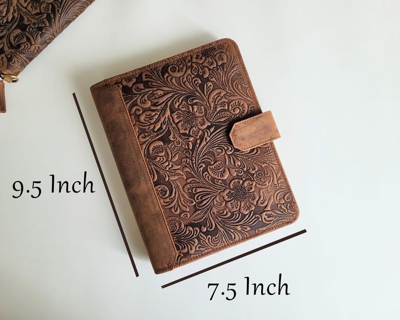 Puede incluir: Un diario de cuero marr&oacute;n con un dise&ntilde;o floral en relieve. El diario mide 24 cm por 19 cm y presenta un cierre de correa de cuero. La cubierta y el lomo son de un marr&oacute;n m&aacute;s oscuro que el dise&ntilde;o floral en relieve.