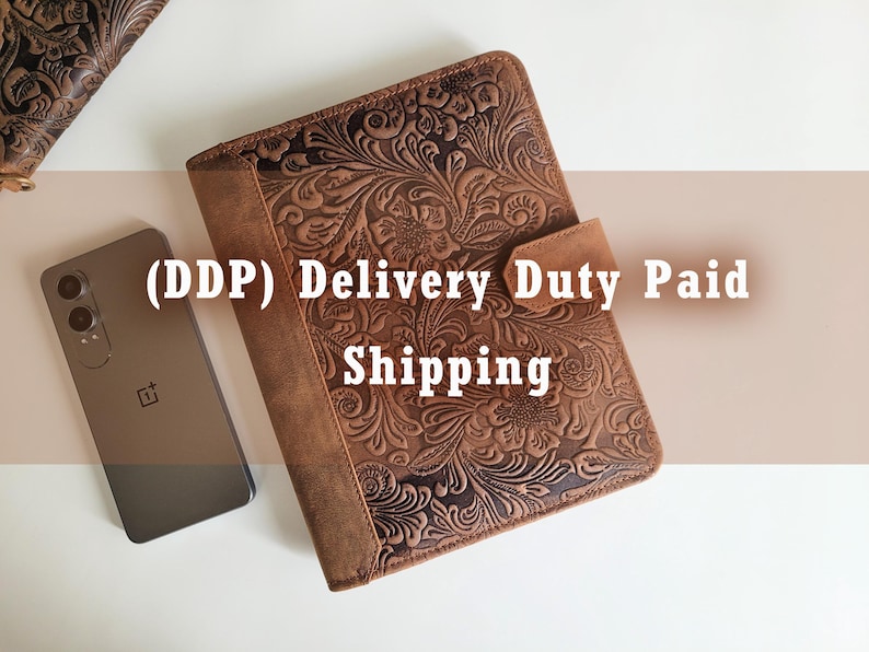 Puede incluir: Un diario de cuero marr&oacute;n con un dise&ntilde;o floral en relieve y un cierre magn&eacute;tico. Un tel&eacute;fono inteligente se coloca junto al diario. El texto en la imagen dice "(DDP) Delivery Duty Paid Shipping".