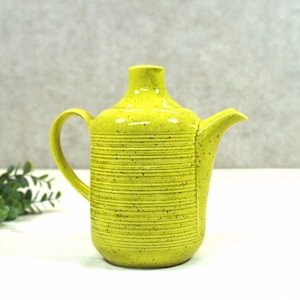 Op de afbeelding: Een gele theepot van keramiek met een gespikkeld glazuur en een geribbeld ontwerp. De theepot heeft een tuit en een handvat.