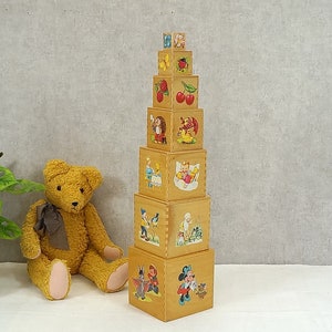 Può includere: Un giocattolo di impilamento in legno con illustrazioni colorate di animali, frutta e bambini. Il giocattolo è composto da otto blocchi, ognuno con un'immagine diversa. I blocchi sono impilati in una torre, con il blocco più grande in basso e il blocco più piccolo in alto.