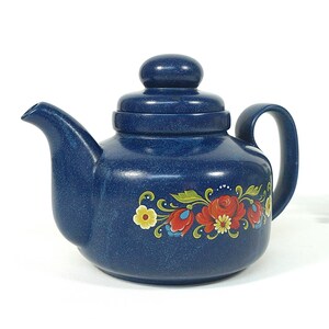 Könnte beinhalten: Eine marineblaue Keramik-Teekanne mit Deckel und Henkel. Die Teekanne hat ein Blumendesign in Rot, Gelb und Grün. Die Teekanne ist ein Küchenartikel.