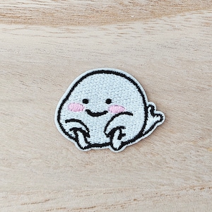 May include: White embroidered patch of a cartoon ghost with pink cheeks and a black outline. The ghost has a simple smile and is sitting with its legs crossed.