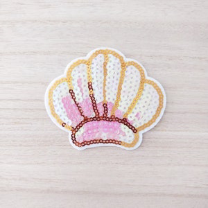 May include: A pink and white seashell-shaped patch with gold sequins. The patch is made of fabric and is perfect for adding a touch of whimsy to clothing or accessories.