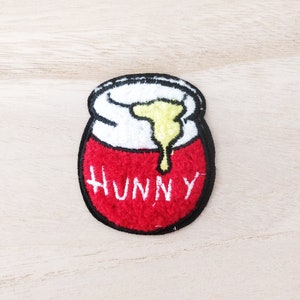 May include: Red and white embroidered iron-on patch with the word "Hunny" and a yellow honey dripping from a jar.