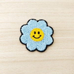 May include: A blue felt flower patch with a yellow smiley face in the centre.
