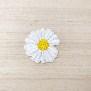 Peut inclure: Patch brodé de couleur blanche représentant une marguerite avec un centre jaune. Le patch est thermocollant et peut être utilisé pour décorer des vêtements, des sacs ou d'autres articles.