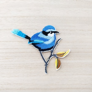 Peut inclure: Patch brodé bleu représentant un oiseau sur une branche avec des feuilles jaunes. L'oiseau est perché sur la branche, les ailes repliées. Ce patch est parfait pour ajouter une touche de nature à vos projets.