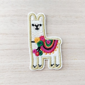 May include: Embroidered llama patch. The white llama has a gold outline and a colourful saddle blanket with pink, green, yellow, and red details. The llama has a black face. A fun, decorative item.