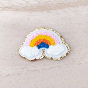Peut inclure: Un patch en feutre en forme de nuage avec un arc-en-ciel aux couleurs vives. L'arc-en-ciel est composé de bandes roses, orange, jaunes et bleues. Le patch est bordé d'une bordure dorée scintillante.