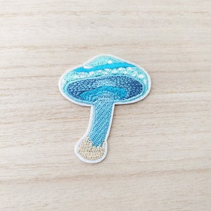 May include: A blue and white embroidered mushroom patch. The mushroom has a light blue stem and a dark blue cap with white dots.