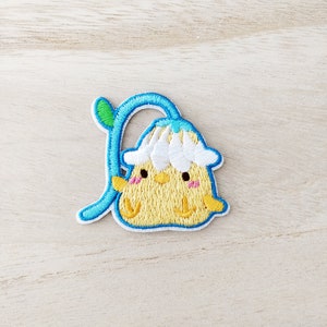May include: An embroidered chick with a white flower on its head, wearing a blue stem with a green leaf. The chick is smiling and has pink cheeks.