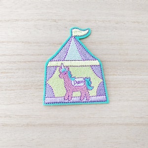 May include: A purple and green embroidered patch of a unicorn inside a tent with a yellow flag.