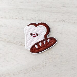 May include: Embroidered iron-on patch featuring a white bread slice with a smiling face and a brown baguette.