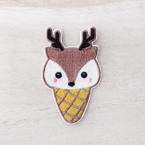 May include: Embroidered iron-on patch of a brown deer with large eyes and antlers, wearing an ice cream cone with a yellow and white waffle pattern.