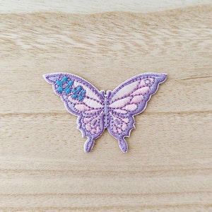 May include: Purple embroidered butterfly patch with pink and blue accents. The butterfly has a delicate design and is perfect for adding a touch of whimsy to clothing or crafts.