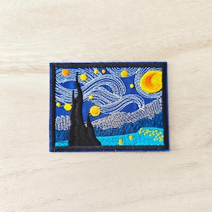 May include: Embroidered patch depicting Van Gogh's "Starry Night." The design features a dark blue sky with swirling white lines, yellow stars, and a crescent moon. A tall, black tree is in the foreground, with a blue border. The patch is square.