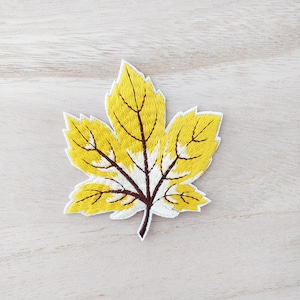 May include: A yellow embroidered leaf patch with brown veins and a white centre. The patch is ideal for adding a touch of autumn to your crafts.