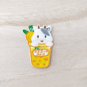 May include: Embroidered iron-on patch featuring a cartoon cow in a yellow cup with the Japanese text "ミルクティー" (milk tea).