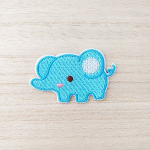 May include: A light blue embroidered elephant patch with white accents. The elephant has a small pink blush on its cheek.