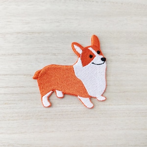 May include: Orange and white embroidered patch of a cartoon corgi dog.