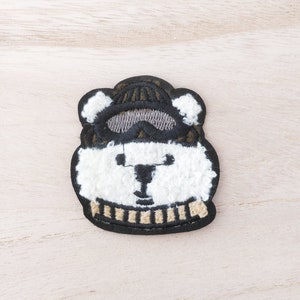 May include: White polar bear embroidered patch with a black hat and goggles, and a brown and white striped scarf.