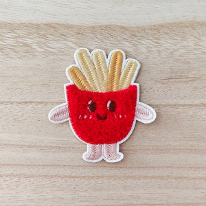 May include: An embroidered patch featuring a cartoon french fry container with a smiling face and arms. The fries are yellow and sticking out of the top of the container.