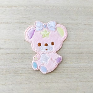 May include: Pink embroidered teddy bear patch with a white bow and a star on its chest. The bear has light blue and purple accents.