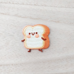 May include: A cute embroidered patch of a smiling slice of bread with orange crust and a white interior. The bread has two small arms and legs.