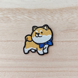 May include: Embroidered iron-on patch of a brown and white Shiba Inu dog wearing a blue bow tie.