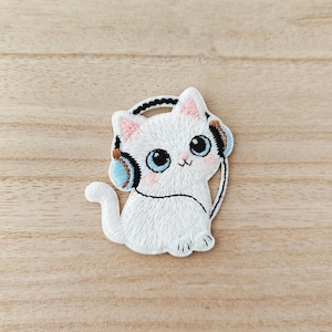 Peut inclure: Écusson brodé d'un chat blanc portant un casque bleu et marron. Le chat a de grands yeux bleus, des joues roses et une queue courbée. Le patch est conçu pour être repassé ou cousu sur du tissu.