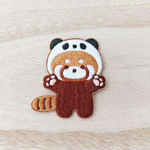 Peut inclure: Patch brodé de panda roux portant un chapeau de panda. Le patch est brun, blanc et noir. Le panda roux est debout, les pattes tendues.
