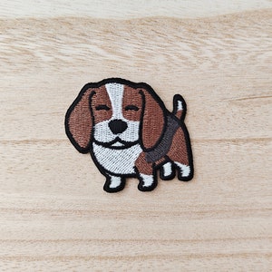 May include: Embroidered iron-on patch of a brown and white beagle with closed eyes. The beagle is standing on all four paws with its tail curled up.